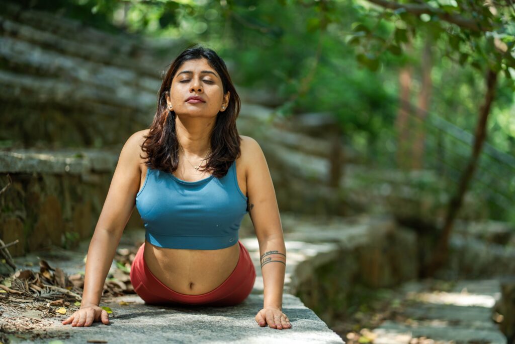 Mujer practicando yoga en un entorno natural, enfocada en la meditación y la respiración, promoviendo bienestar físico y mental.