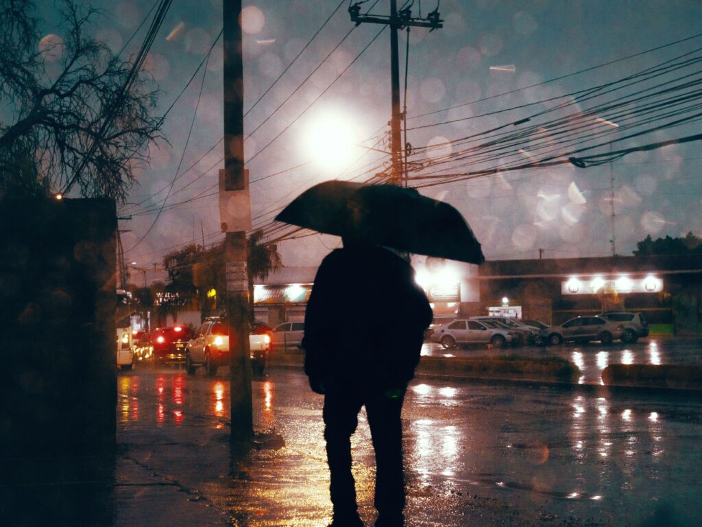 Persona con paraguas bajo la lluvia en una calle de la Ciudad de México, con luces de vehículos reflejadas en el pavimento.