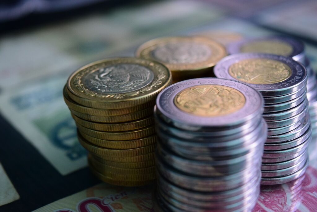 Monedas y billetes de pesos mexicanos apilados, representando el contexto económico y la inflación en México.