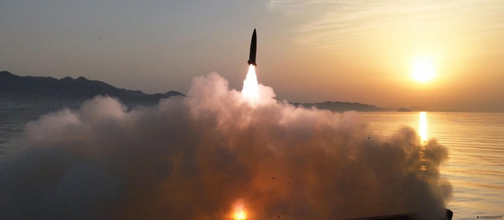 Lanzamiento de un misil balístico desde la costa de Corea del Norte, con humo y fuego visible al atardecer.