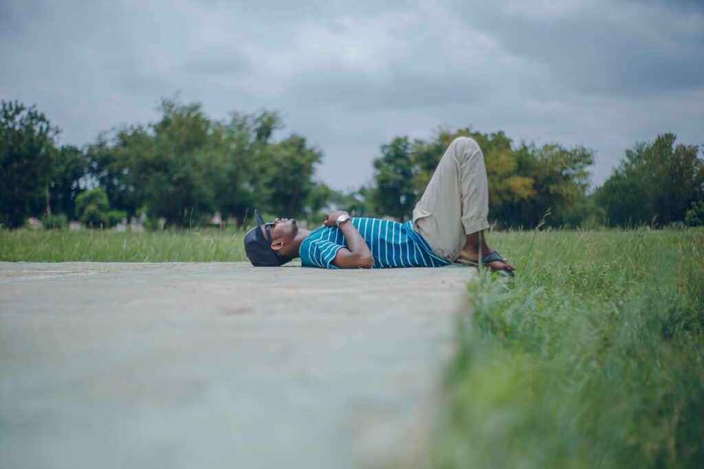 Hombre relajándose en un campo, acostado sobre el suelo, disfrutando de un domingo tranquilo y desconectado del trabajo.